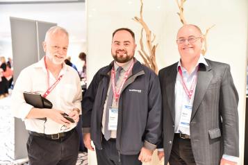 Three men, two of which have beards, standing at an indoor event