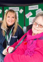 Healthwatch Volunteer at a community event speaking to a woman in a wheelchair